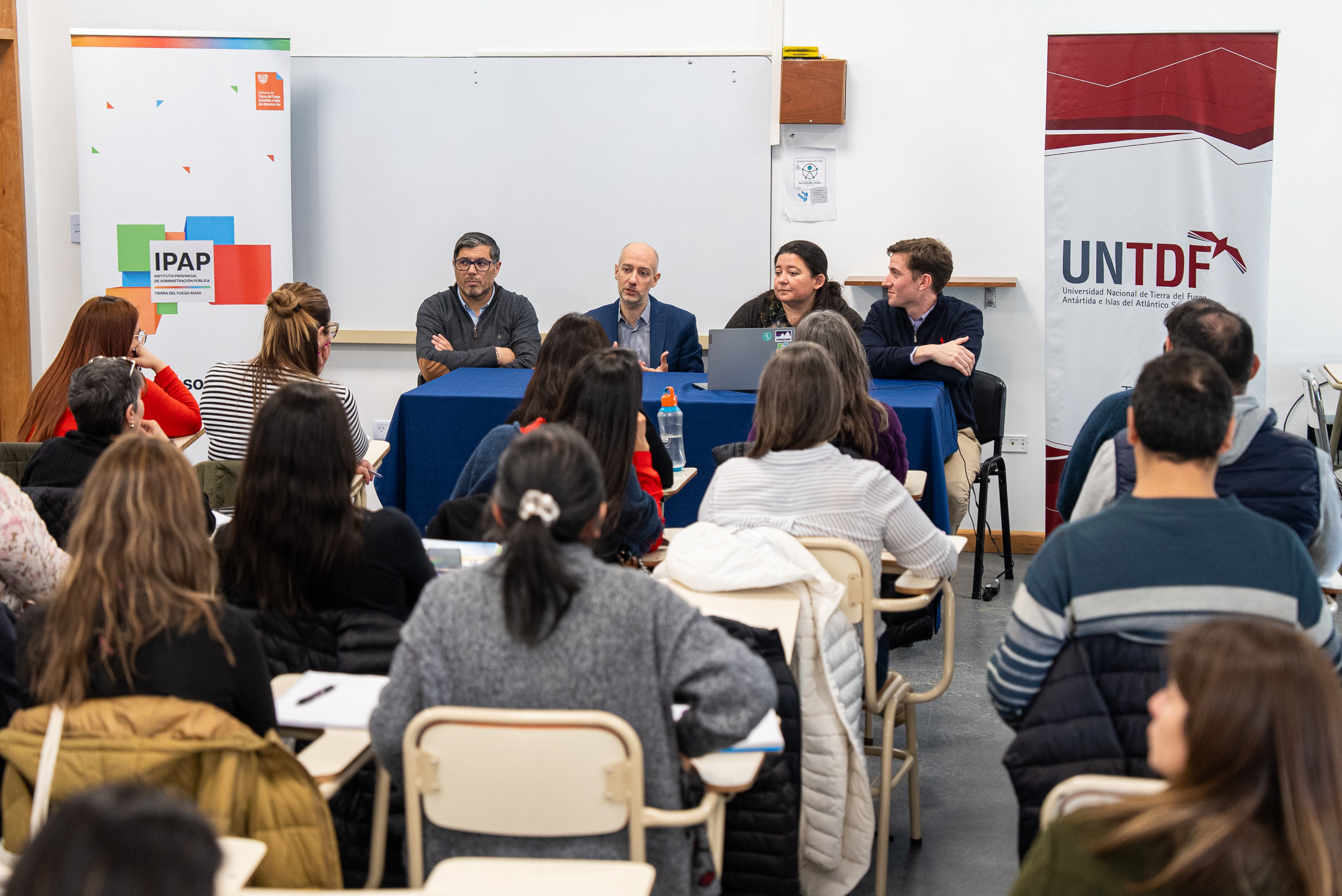 toma desde atrás en un aula de universidad, cuatro personas dando una conferencia