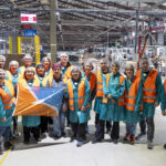 personas con chaleco de seguridad en una fábrica posando con una bandera de tierra del fuego