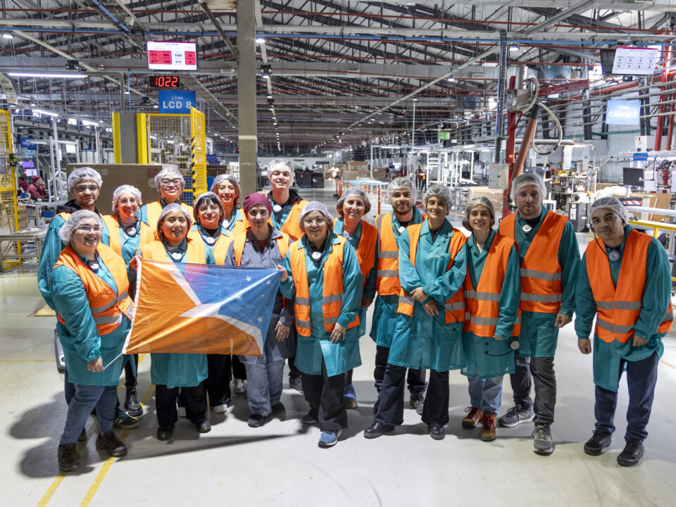 personas con chaleco de seguridad en una fábrica posando con una bandera de tierra del fuego